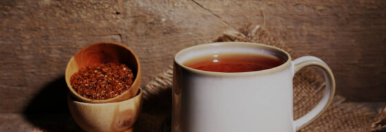 Kubek z zaparzoną herbatą rooibos i dwie drewniane miseczki pełne herbaty.