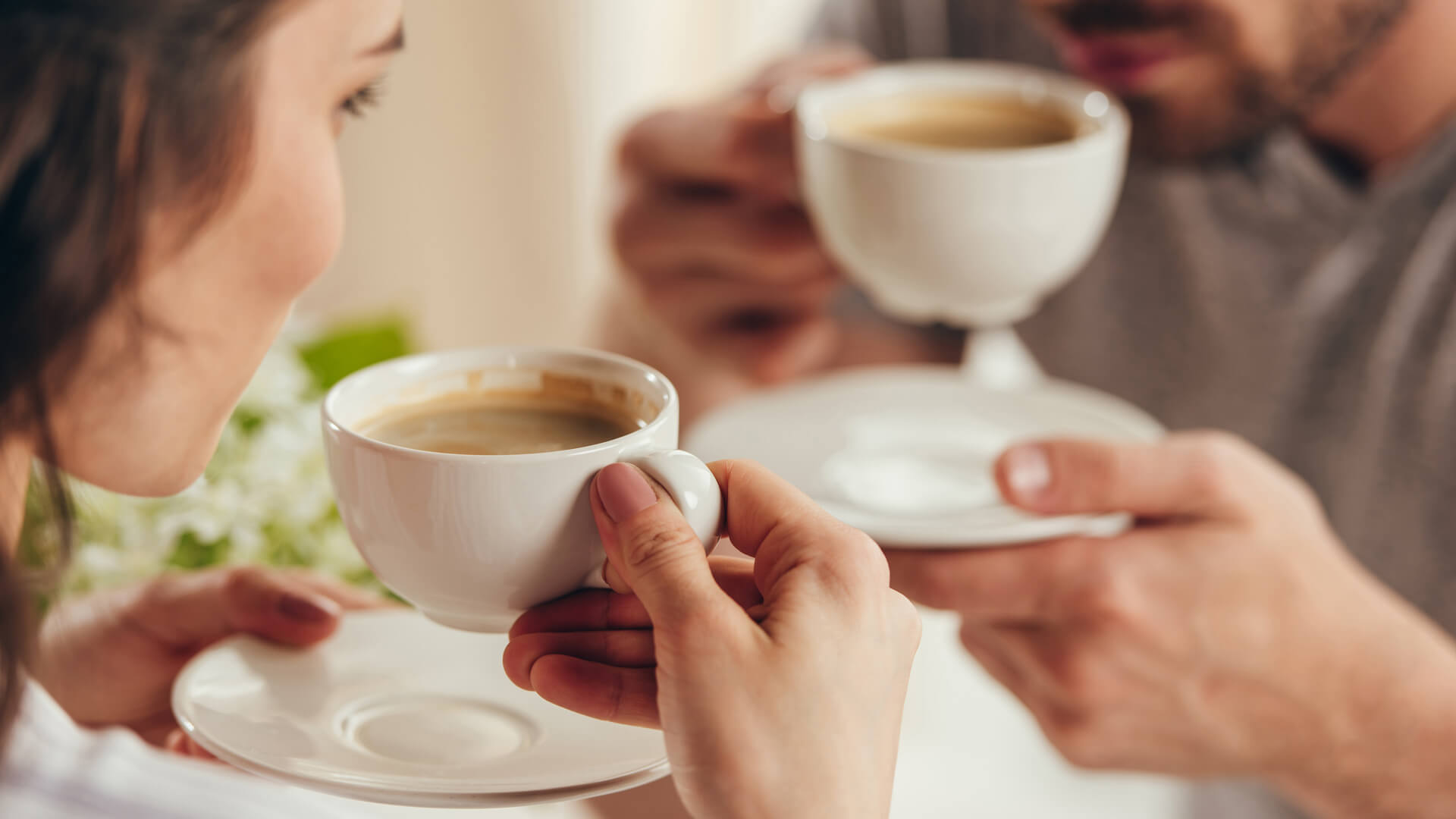 Dwoje ludzi pijących kawę z białych filiżanek, zbliżenie na ręce i napoje podczas wspólnej chwili.