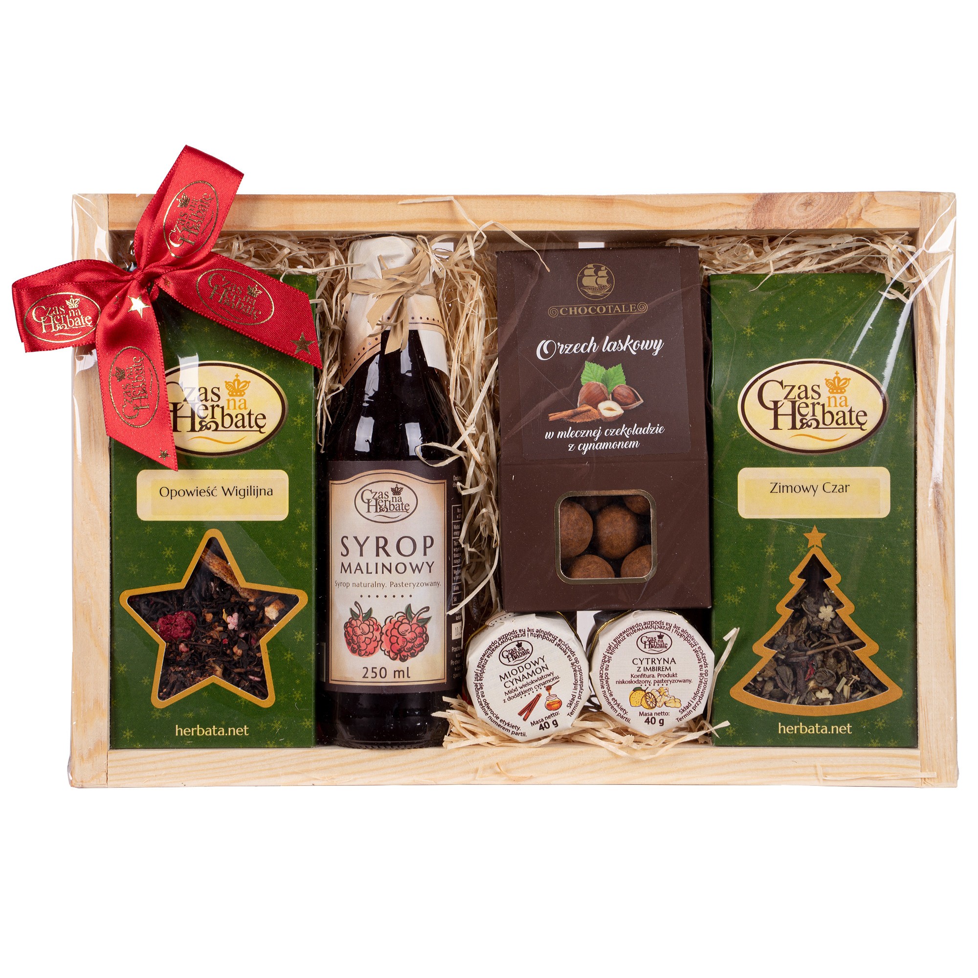Drewniana skrzynka z czerwoną kokardą, w środku zielone opakowanie herbaty z okienkiem w kształcie gwiazdy, szklana butelka soku malinowego, opakowanie orzechów laskowych w czekoladzie, słoiczek miodowego cynamonu, słoiczek cytryny z imbirem oraz zielone opakowanie herbaty z okienkiem w kształcie choinki