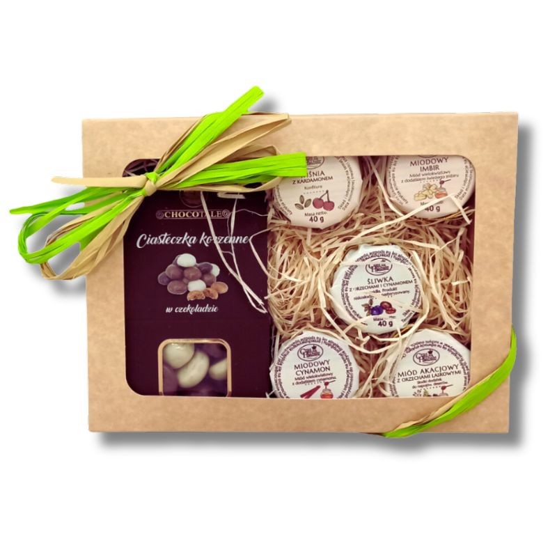 Beżowy kartonik obwiązany zieloną wstążką, w środku opakowanie ciasteczek korzennych oraz pięć słoiczków