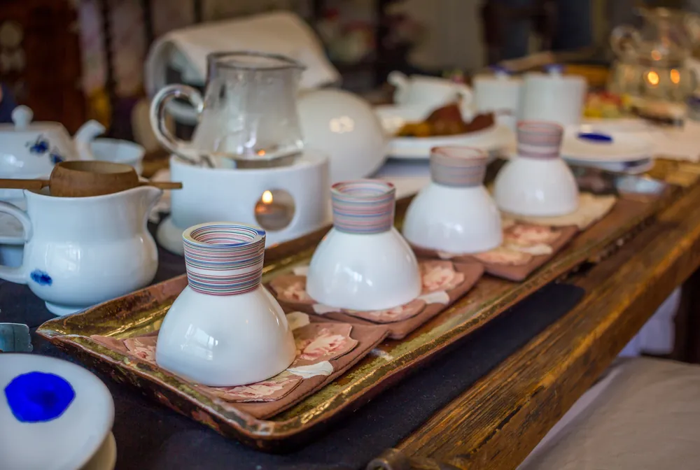 Cztery porcelanowe czarki do herbaty odwrócone do góry dnem na ozdobnych podstawkach, na tle akcesoriów.