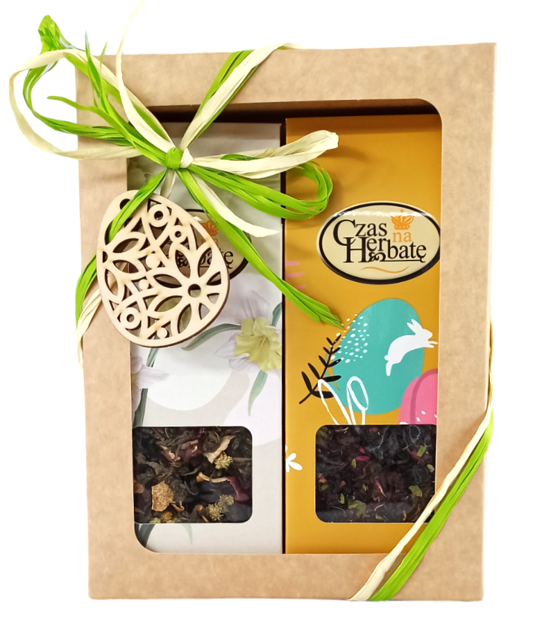 Beżowy karton z okienkiem, zieloną wstążką i drewnianym ażurowym jajkiem wielkanocnym, w środku dwa opakowania herbaty