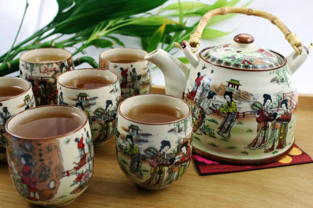 Zestaw do herbaty w stylu orientalnym: czajnik z bambusową rączką i sześć filiżanek z naparem.