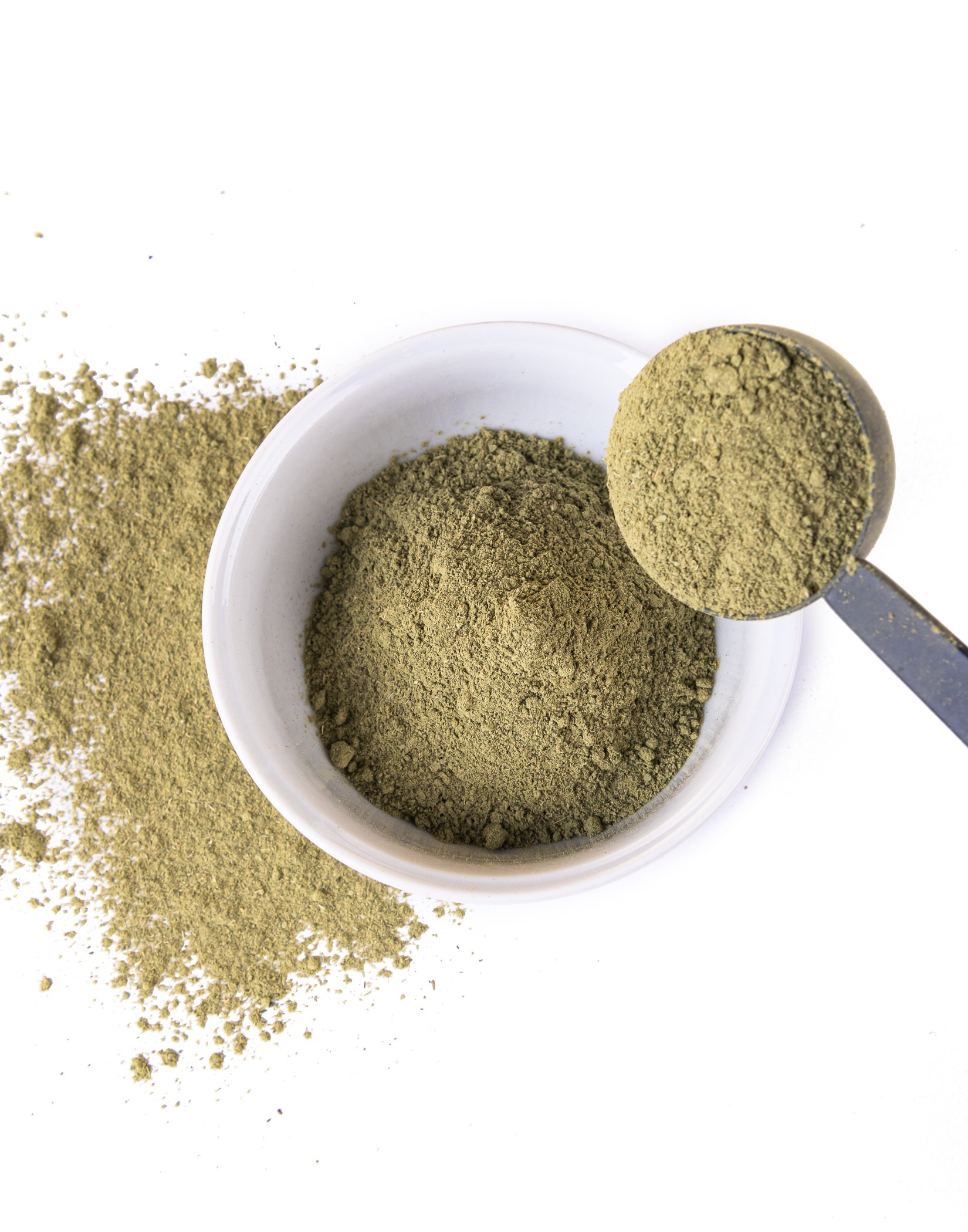 Biała miska z zielonym proszkiem, obok rozlany proszek i metalowa łyżka z porcją proszku.