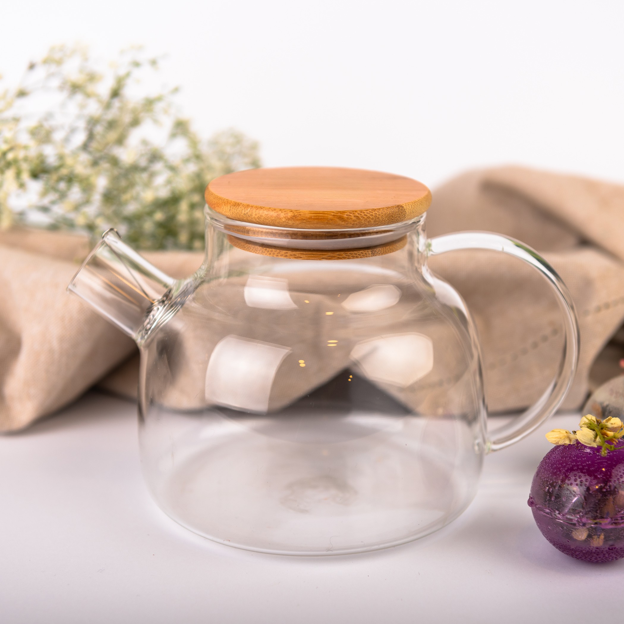 Glass teapot with bamboo lid, empty inside. On the right a decorative purple flower tea ball.