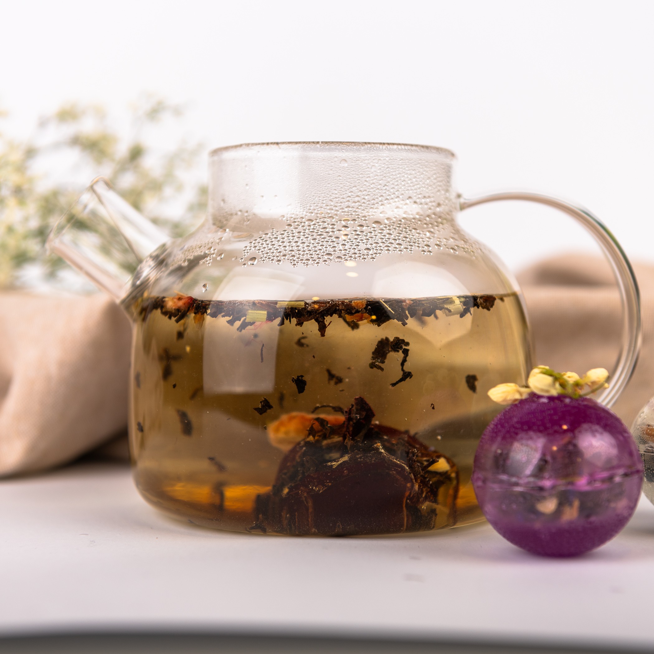 Szklana kula do parzenia herbaty w kolorze bursztynowym, ozdobiona dużą liofilizowaną truskawką.