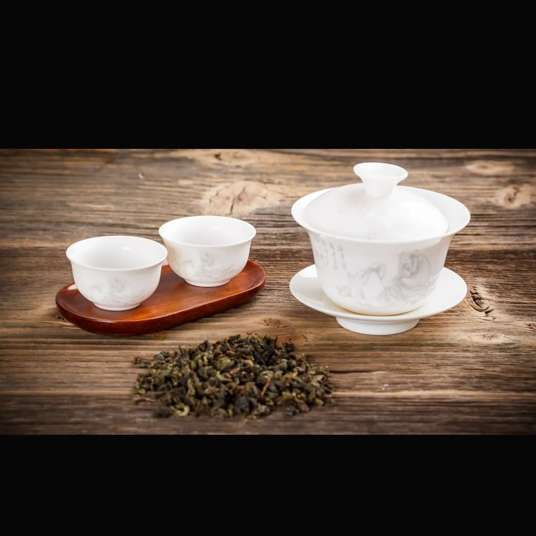 Sypana liściasta herbata, dwie białe czarki na drewnianej podstawce, biały dzbanek na stole.