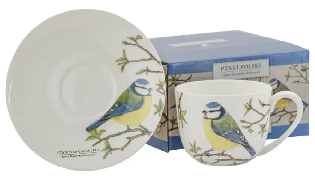 Filiżanka ze spodkiem z malunkiem sikory modrej na gałązce, w tle niebieskie pudełko z tym samym motywem.