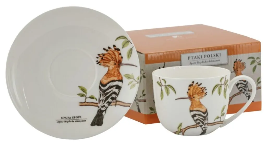 Filiżanka i spodek z ilustracją dudka na gałęzi, w tle pomarańczowe pudełko z tym samym motywem.