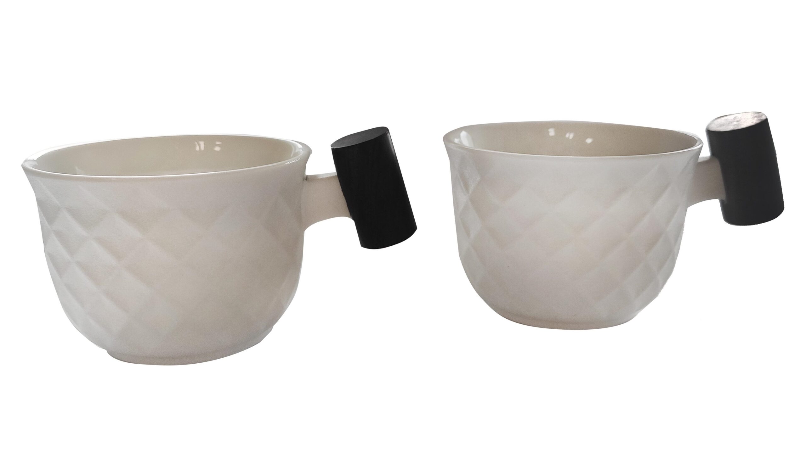 Dwie nowoczesne filiżanki z jasnej ceramiki o tłoczonej fakturze, wyposażone w oryginalne czarne, walcowate uchwyty.