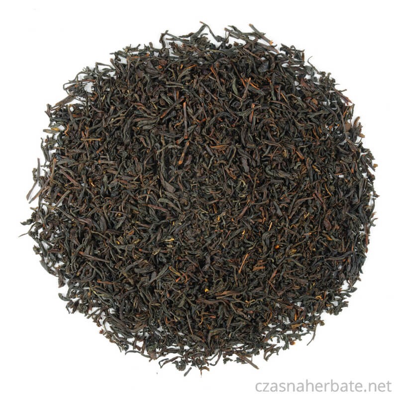 Luźna, czarna herbata liściasta o drobnych, poskręcanych listkach, rozsypana na białym tle.