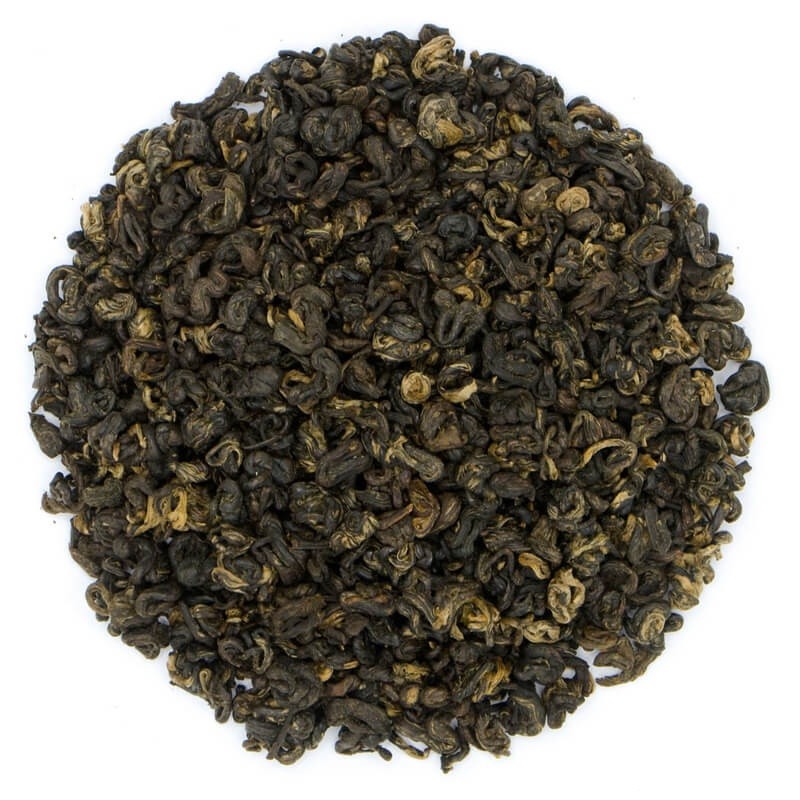 Luźne liście zielonej herbaty gunpowder, zwartę i zrolowane, ułożone w okrąg na białym tle.