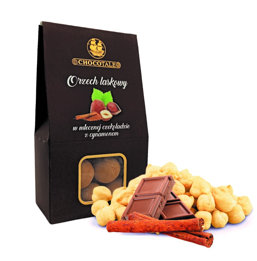 Pudełko Chocotale orzech laskowy, otoczone czekoladą, orzechami laskowymi i laskami cynamonu na białym tle.