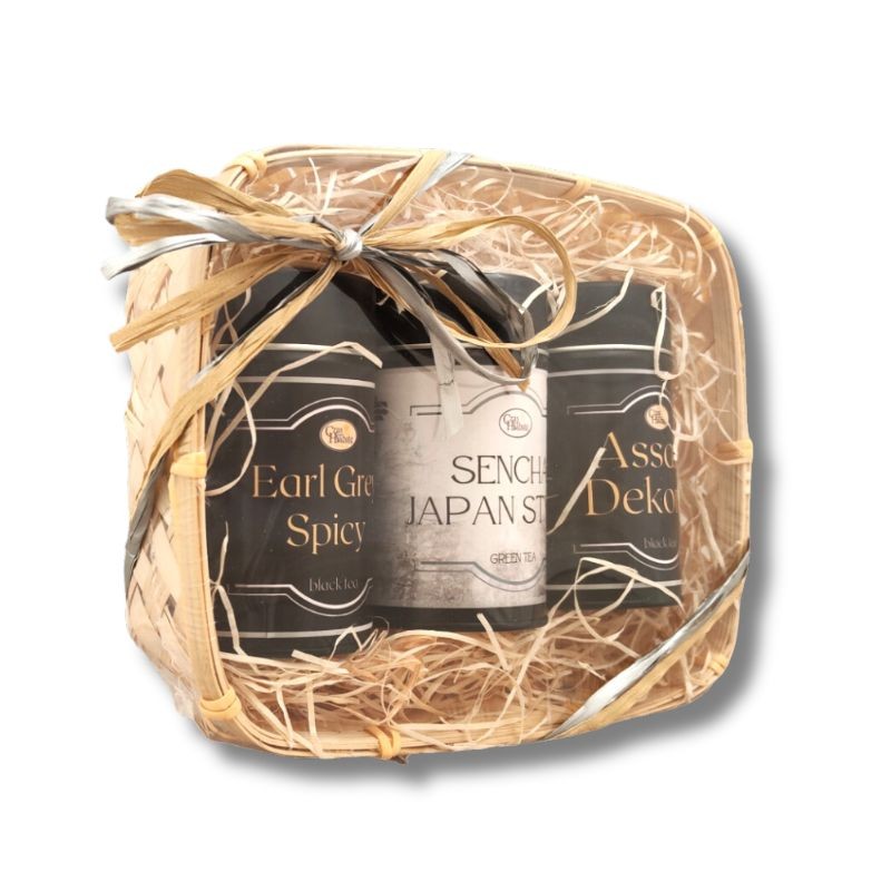 Widok z boku na kosz prezentowy z trzema puszkami herbaty: Earl Grey Spicy, Sencha Japan Style i Assam Dekorai, ozdobiony wstążką.