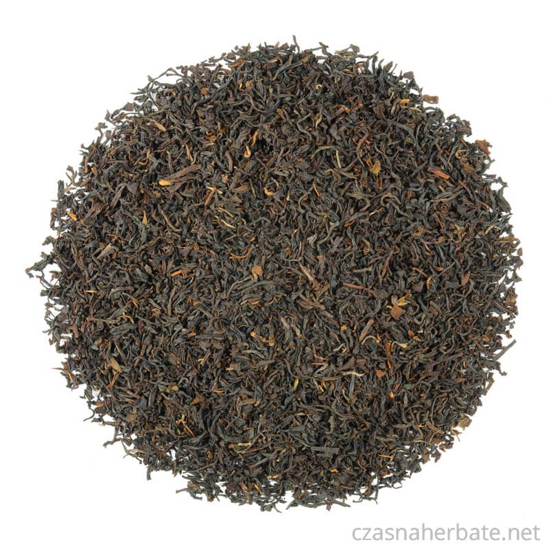 Sypana czarna herbata Assam o drobnych ciemnych liściach, rozrzucona na białym tle.