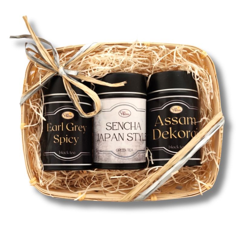 Widok z przodu na kosz prezentowy z trzema puszkami herbaty: Earl Grey Spicy, Sencha Japan Style i Assam Dekorai, ozdobiony wstążką.