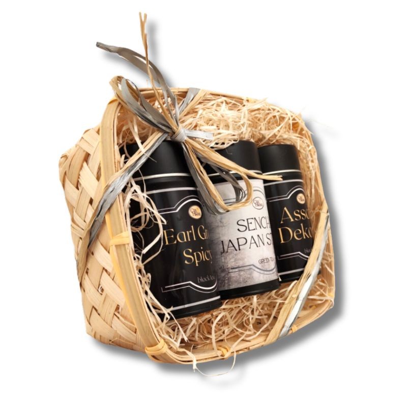 Widok z boku na kosz prezentowy z trzema puszkami herbaty: Earl Grey Spicy, Sencha Japan Style i Assam Dekorai, ozdobiony wstążką.