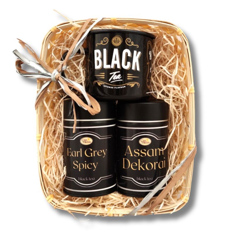 WIdok z przodu na kosz prezentowy z trzema czarnymi puszkami herbaty: Black Tea, Earl Grey Spicy i Assam Dekorai, ozdobiony wstążką.