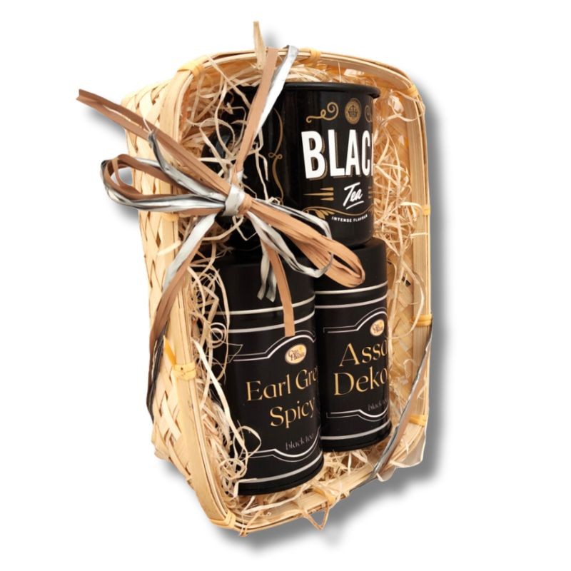 WIdok z boku na kosz prezentowy z trzema czarnymi puszkami herbaty: Black Tea, Earl Grey Spicy i Assam Dekorai, ozdobiony wstążką.
