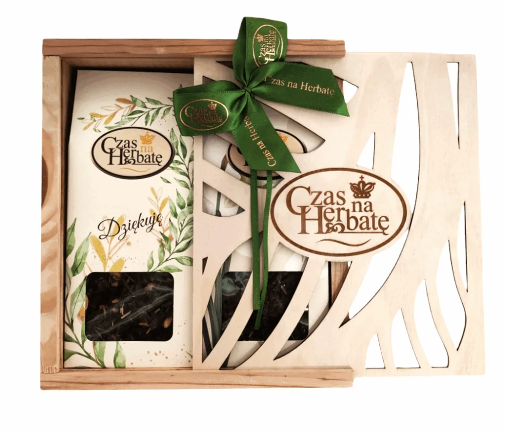 Widok z przodu na otwartą, drewnianą skrzynkę prezentową z ozdobnym wycinanym frontem i zieloną satynową kokardą, w środku widoczne produkty marki.