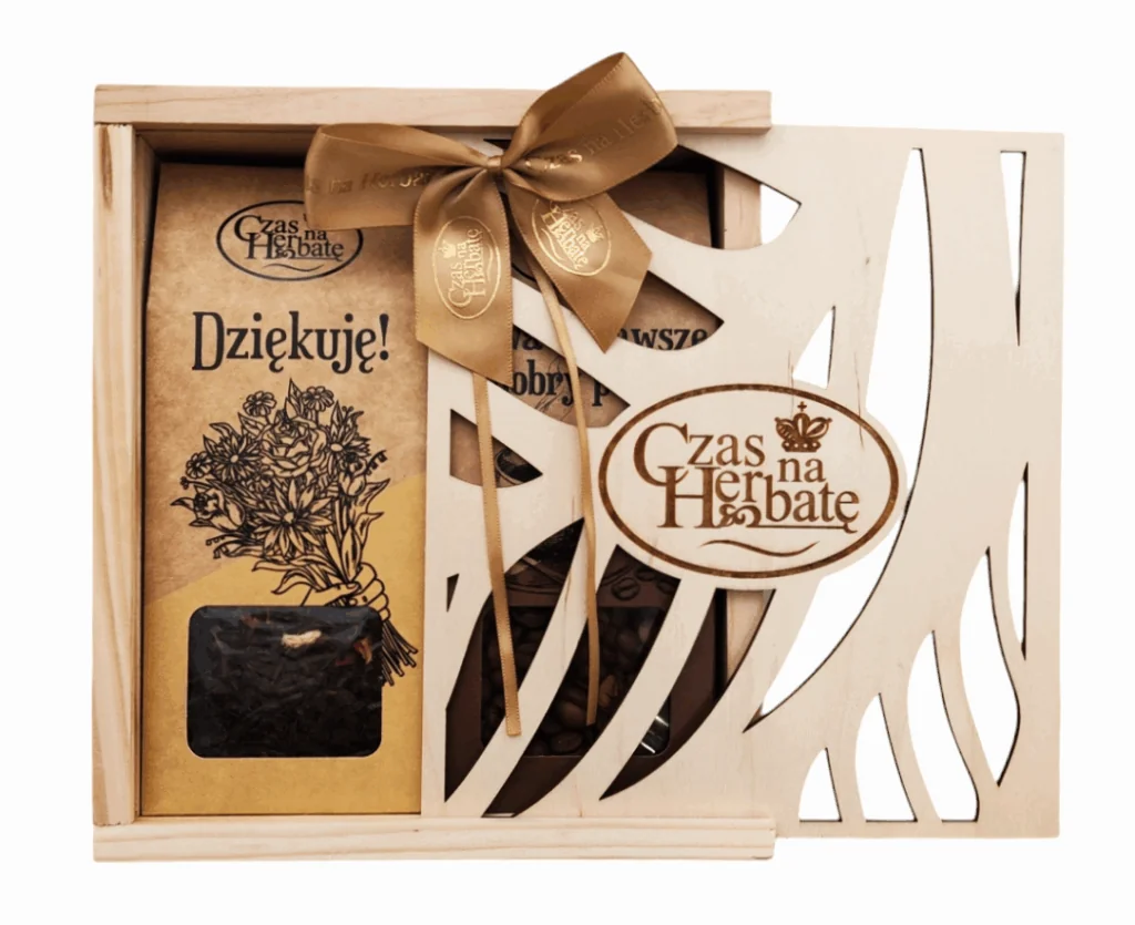 Widok z przodu na otwartą, drewnianą skrzynkę prezentową „Czas na Herbatę” z ozdobną wycinanką i satynową kokardą, wewnątrz widoczne herbaty.