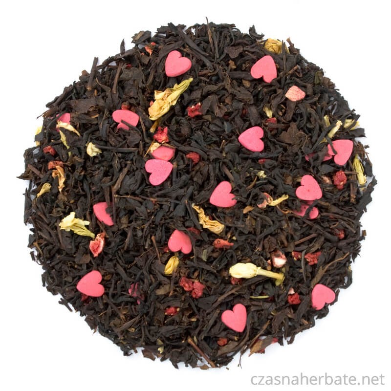 Czarna herbata z dodatkiem żółtych kwiatów, kawałków suszonych owoców oraz różowych cukrowych serduszek, dekoracyjna mieszanka widziana z góry.