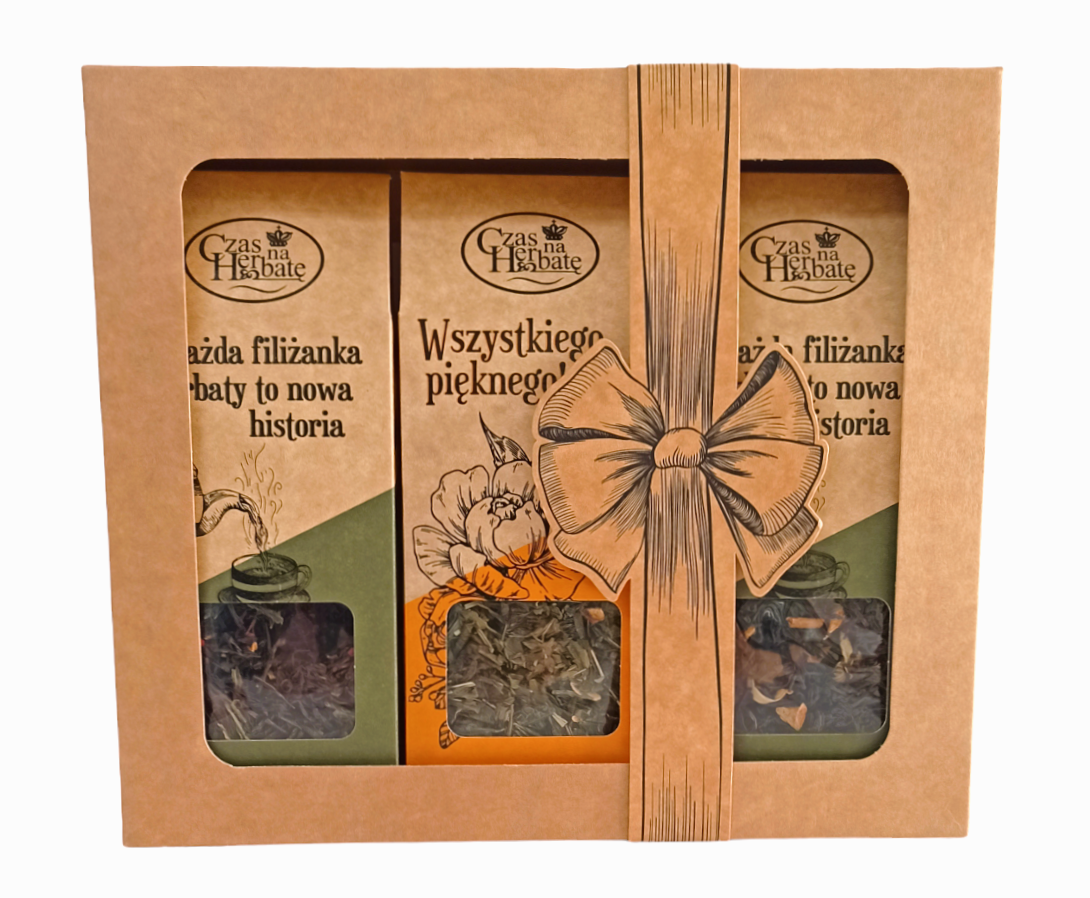 Zestaw herbat w kartonowym opakowaniu z okienkiem i nadrukowaną wstążką z kokardą; widoczne trzy torebki herbaty o dekoracyjnych etykietach.