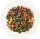 On a white plate lies a mixture of green tea with pieces of dried strawberries and flower petals.