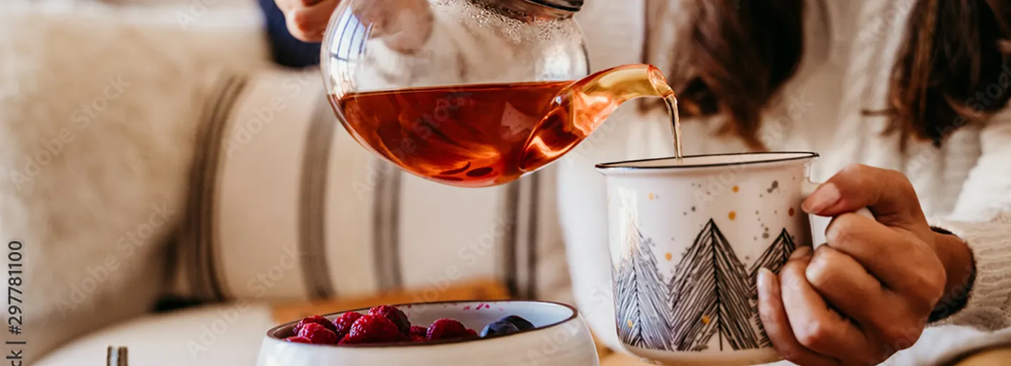 Nalewanie herbaty z szklanego dzbanka do białego kubka w górski wzór, w ciepłym, domowym otoczeniu