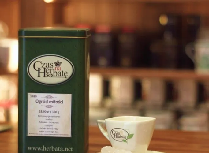 Puszka herbaty ‘Ogród miłości’ marki Czas na Herbatę oraz filiżanka z logo sklepu na drewnianym blacie w sklepie herbacianym