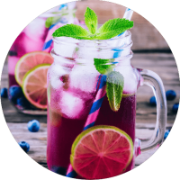 Herbata owocowa Malinowa Rapsodia, na zimno, w szklanym kubku z uchem. Do herbaty dodany lód, borówki, plastry limonki i mięta.